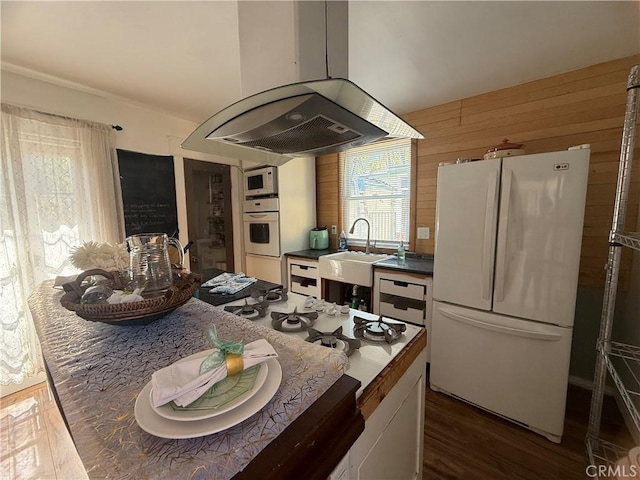 kitchen featuring wooden walls, white appliances, a sink, dark countertops, and island exhaust hood