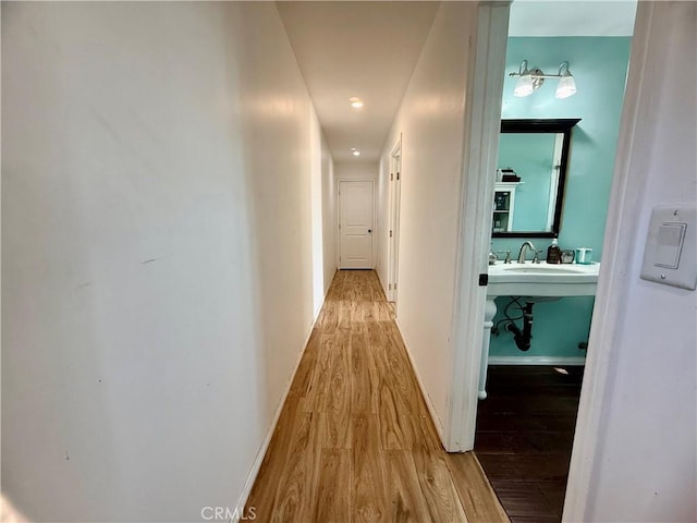 hall with a sink, wood finished floors, and baseboards