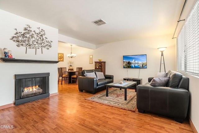 living area featuring visible vents, baseboards, a lit fireplace, light wood-style floors, and a notable chandelier