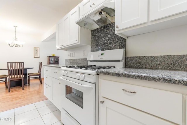 kitchen with light tile patterned floors, an inviting chandelier, white cabinets, under cabinet range hood, and white gas range