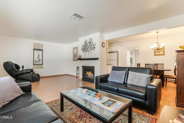 living area with visible vents, a notable chandelier, a warm lit fireplace, and light wood finished floors