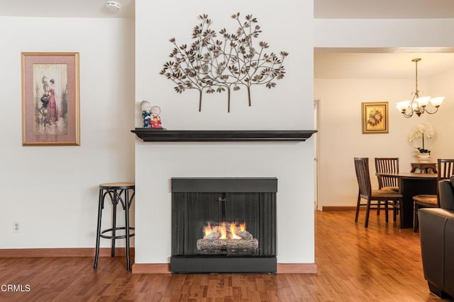 interior details with baseboards, wood finished floors, a warm lit fireplace, and a chandelier