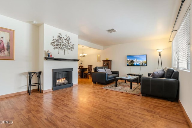 living area with visible vents, baseboards, a chandelier, a multi sided fireplace, and light wood-style flooring