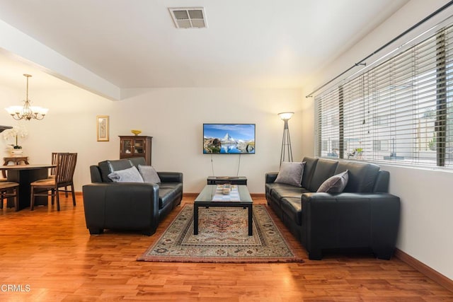 living area featuring visible vents, baseboards, beamed ceiling, light wood-style flooring, and a notable chandelier