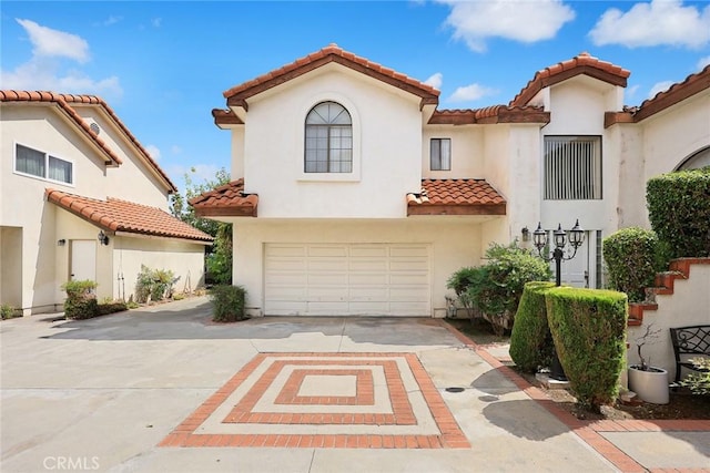 mediterranean / spanish-style house with a garage, driveway, a tiled roof, and stucco siding