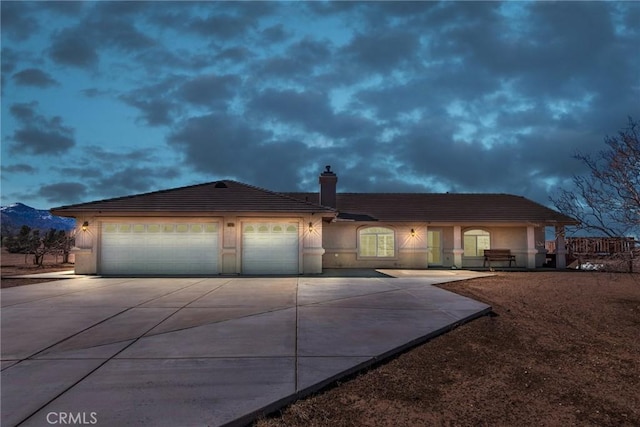 view of front facade featuring driveway, a chimney, an attached garage, and stucco siding