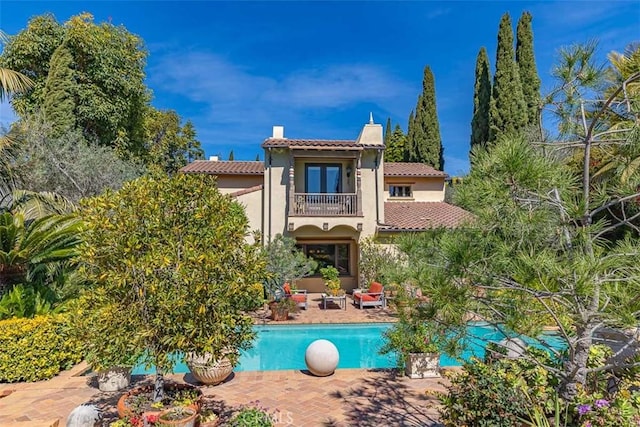 rear view of house featuring a tile roof, a patio area, a chimney, stucco siding, and a balcony