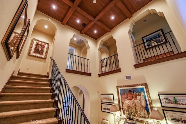 stairs featuring wooden ceiling, beam ceiling, a high ceiling, visible vents, and recessed lighting