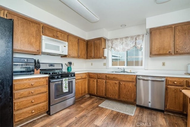 kitchen with appliances with stainless steel finishes, brown cabinetry, a sink, and dark wood finished floors