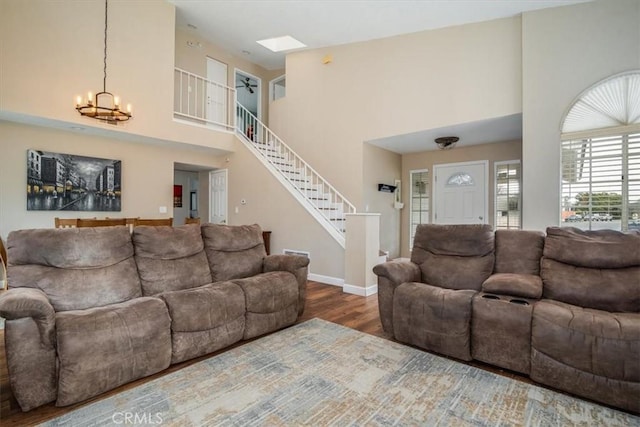 living area featuring baseboards, a towering ceiling, stairway, wood finished floors, and an inviting chandelier