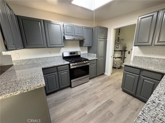 kitchen with light wood-style flooring, under cabinet range hood, a skylight, water heater, and stainless steel range with gas stovetop