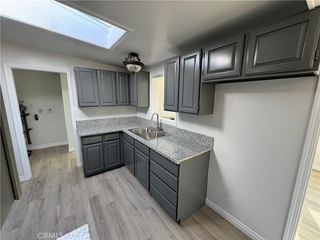 kitchen featuring baseboards, light wood finished floors, a sink, and gray cabinetry