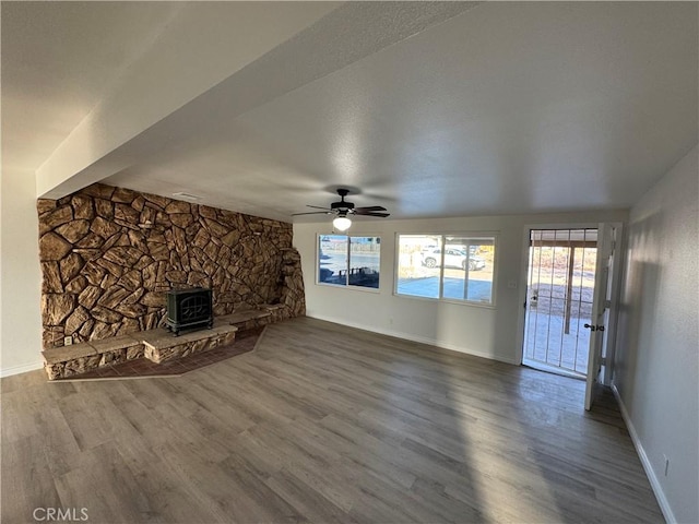 unfurnished living room featuring a wood stove, ceiling fan, baseboards, and wood finished floors