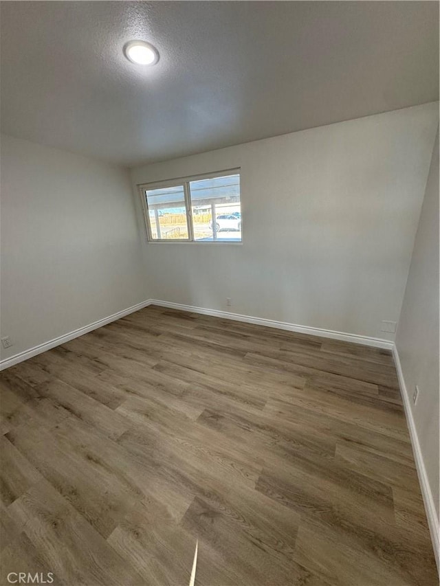 empty room with a textured ceiling, baseboards, and wood finished floors