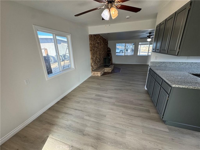 interior space with a wood stove, light wood-style flooring, baseboards, and ceiling fan