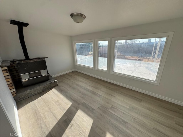 living area with plenty of natural light, wood finished floors, a wood stove, and baseboards