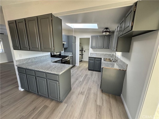 kitchen with stainless steel gas range oven, a peninsula, a sink, baseboards, and light wood-style floors