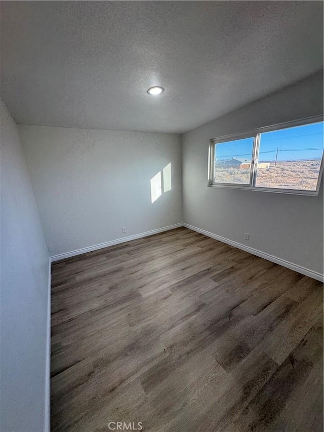 unfurnished room featuring a textured ceiling, wood finished floors, and baseboards