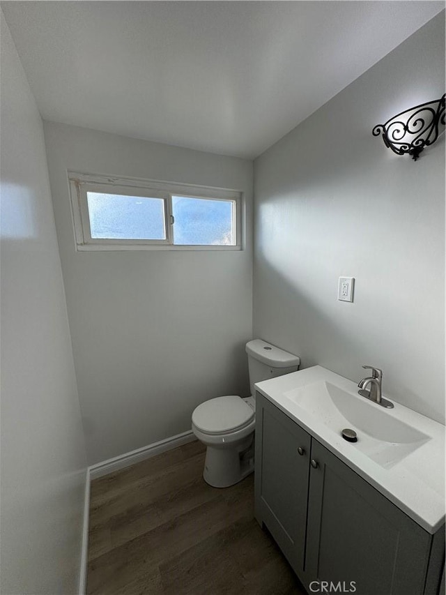 bathroom featuring toilet, baseboards, wood finished floors, and vanity