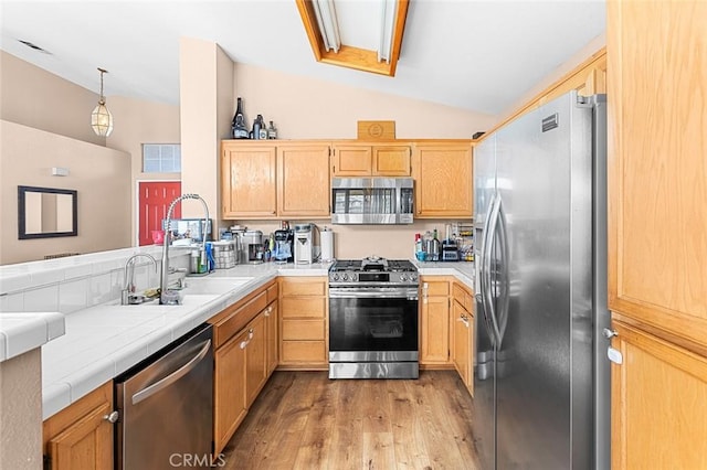 kitchen with lofted ceiling, light wood-style flooring, a peninsula, appliances with stainless steel finishes, and tile counters