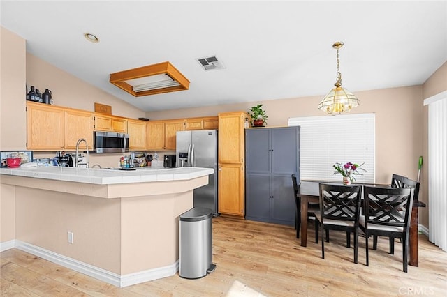 kitchen featuring decorative light fixtures, tile counters, appliances with stainless steel finishes, light wood-style floors, and a peninsula