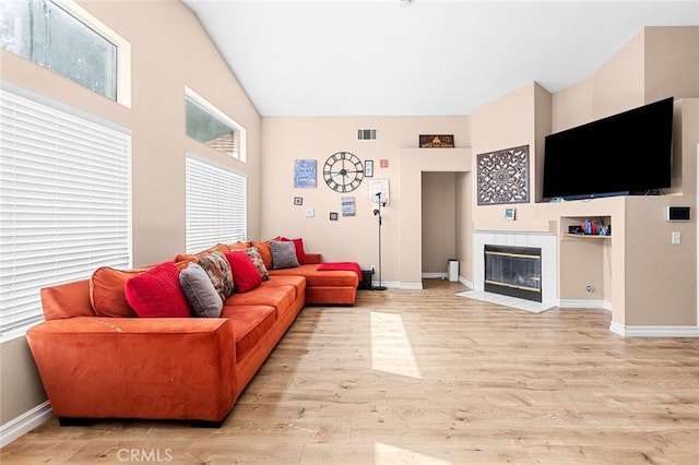 living room featuring baseboards, a tile fireplace, visible vents, and light wood-style floors