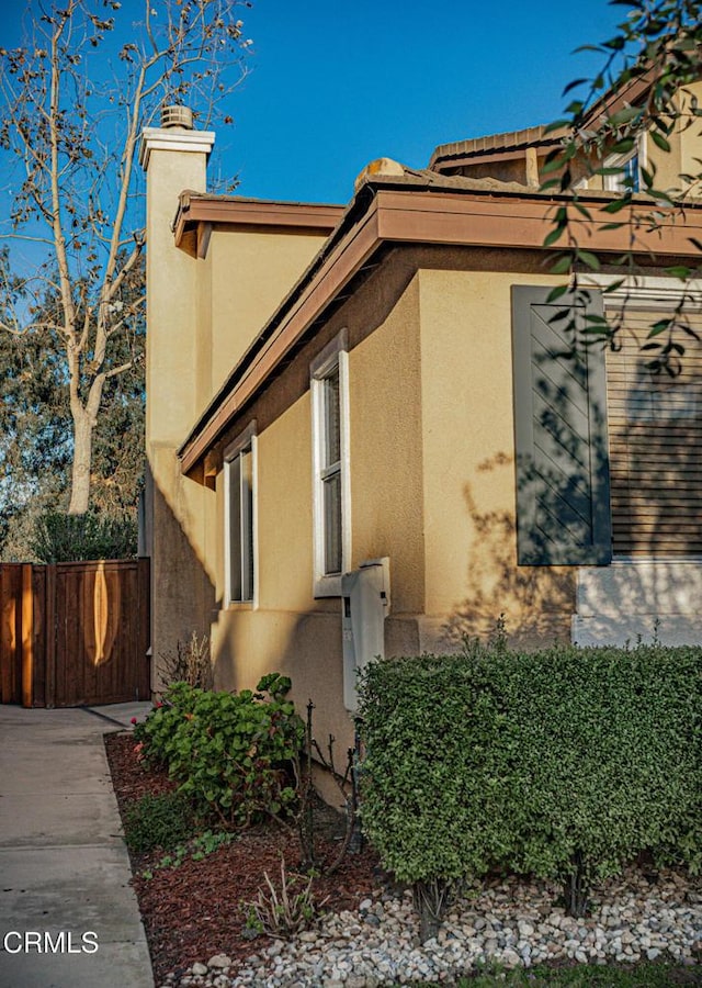 view of property exterior with a chimney, fence, and stucco siding