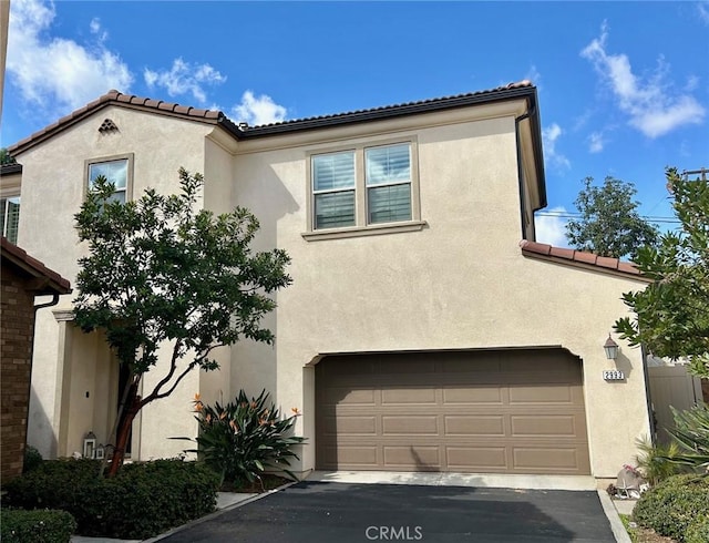 mediterranean / spanish-style house featuring an attached garage, a tiled roof, and stucco siding