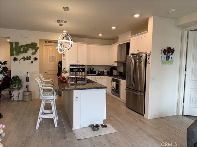 kitchen with visible vents, appliances with stainless steel finishes, white cabinetry, wall chimney exhaust hood, and light wood-type flooring