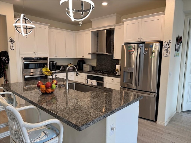 kitchen with light wood finished floors, a sink, white cabinets, appliances with stainless steel finishes, and wall chimney exhaust hood