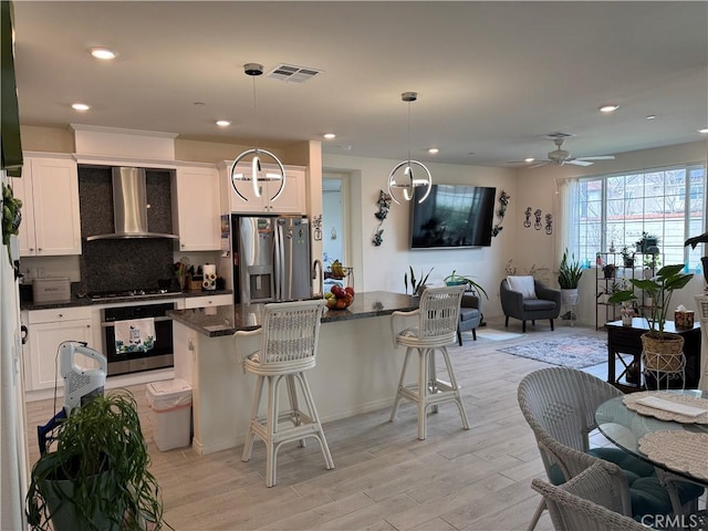 kitchen with visible vents, stainless steel appliances, a kitchen bar, wall chimney range hood, and open floor plan