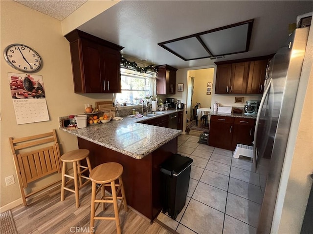 kitchen featuring a breakfast bar area, light stone countertops, a peninsula, freestanding refrigerator, and a sink