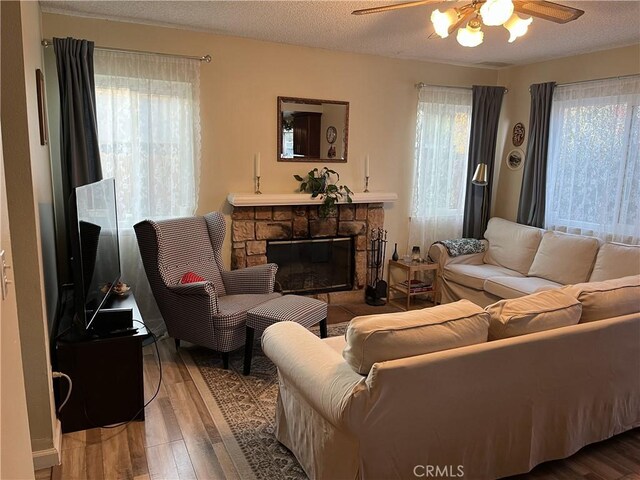 living room with a fireplace, a ceiling fan, wood finished floors, and a textured ceiling