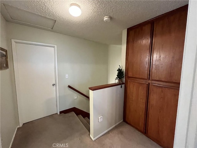 corridor featuring baseboards, attic access, a textured ceiling, an upstairs landing, and light colored carpet