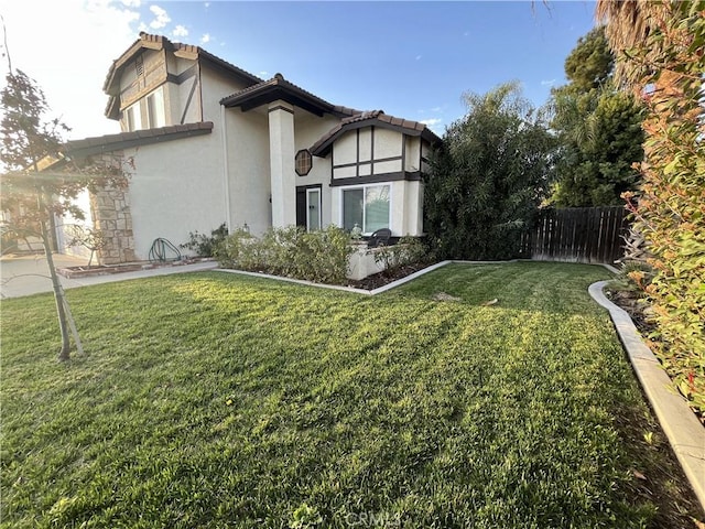 exterior space featuring fence, a tile roof, stucco siding, a lawn, and a patio