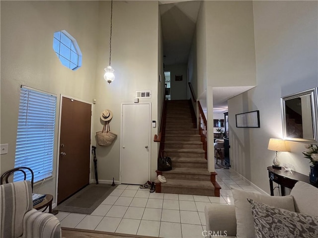 interior space featuring visible vents, baseboards, stairway, light tile patterned floors, and a high ceiling