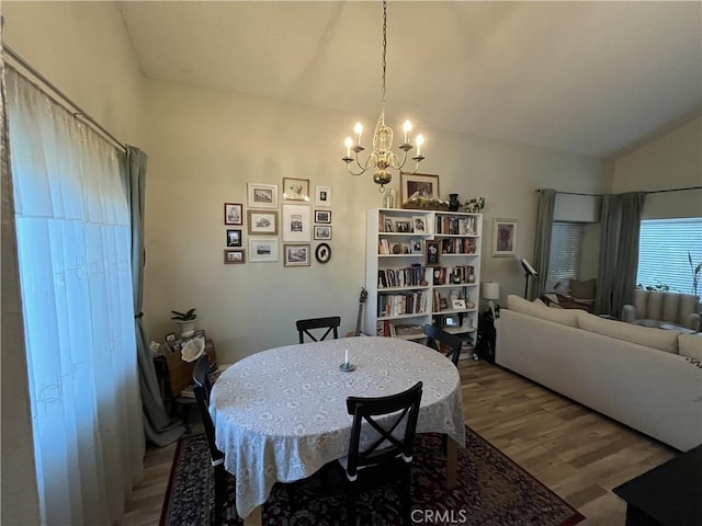 dining room with an inviting chandelier, vaulted ceiling, and wood finished floors