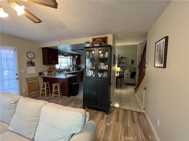 living area with a textured ceiling, light wood finished floors, baseboards, ceiling fan, and stairs