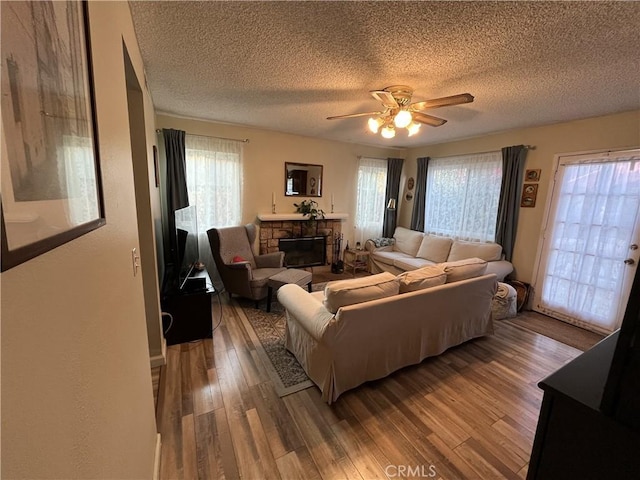 living room featuring a fireplace, a ceiling fan, wood finished floors, and a textured ceiling