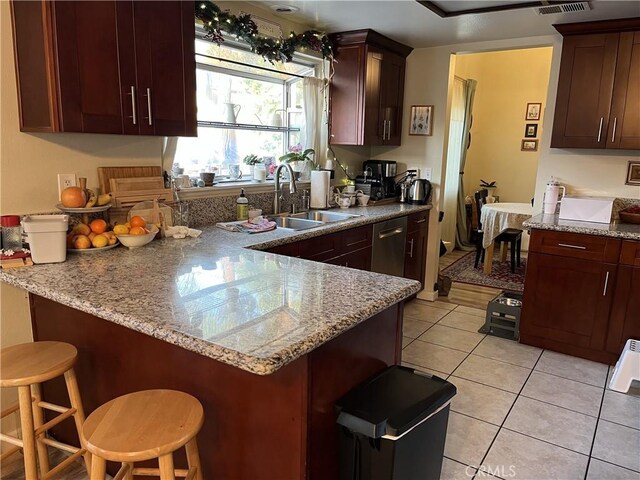 kitchen with light stone counters, light tile patterned floors, a peninsula, a sink, and a kitchen bar