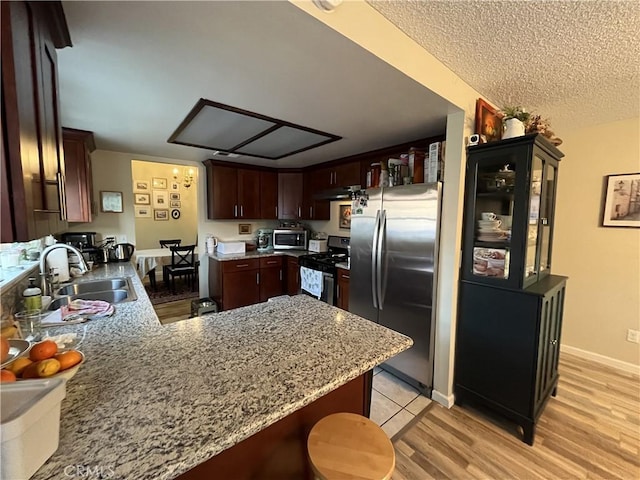 kitchen with light wood-style flooring, appliances with stainless steel finishes, a peninsula, a textured ceiling, and a sink