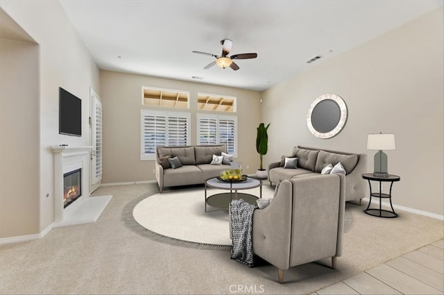 carpeted living room with baseboards, a glass covered fireplace, visible vents, and a ceiling fan