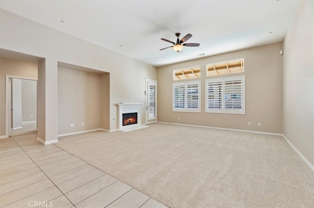 unfurnished living room featuring visible vents, a ceiling fan, light carpet, a warm lit fireplace, and baseboards