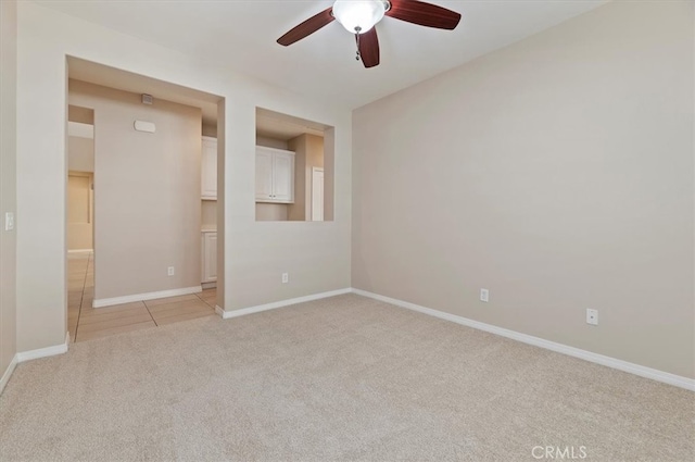 empty room featuring baseboards, light tile patterned flooring, a ceiling fan, and light colored carpet