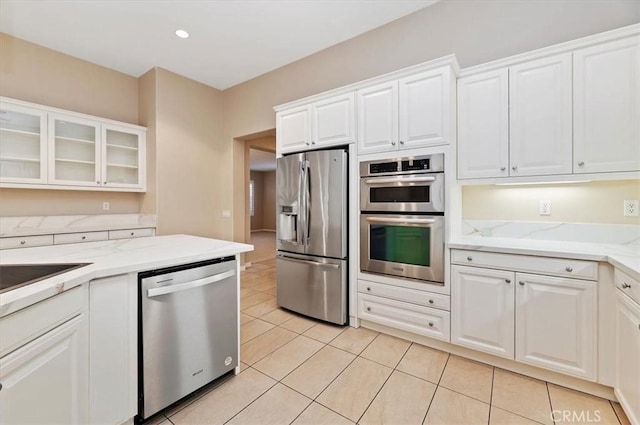 kitchen featuring light tile patterned floors, stainless steel appliances, glass insert cabinets, white cabinets, and light stone countertops