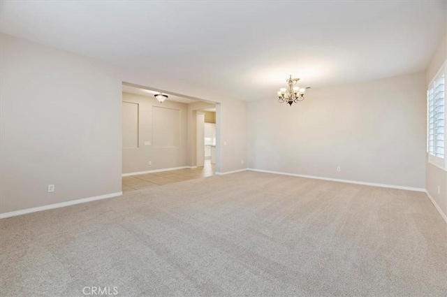 spare room featuring light colored carpet, a notable chandelier, and baseboards