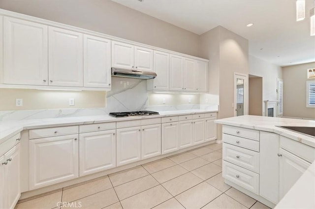 kitchen with white cabinets, stainless steel gas stovetop, under cabinet range hood, and light tile patterned floors