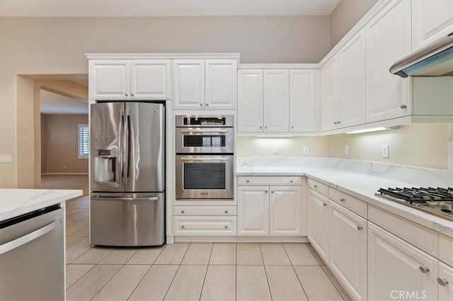 kitchen featuring white cabinets, appliances with stainless steel finishes, light stone countertops, under cabinet range hood, and light tile patterned flooring