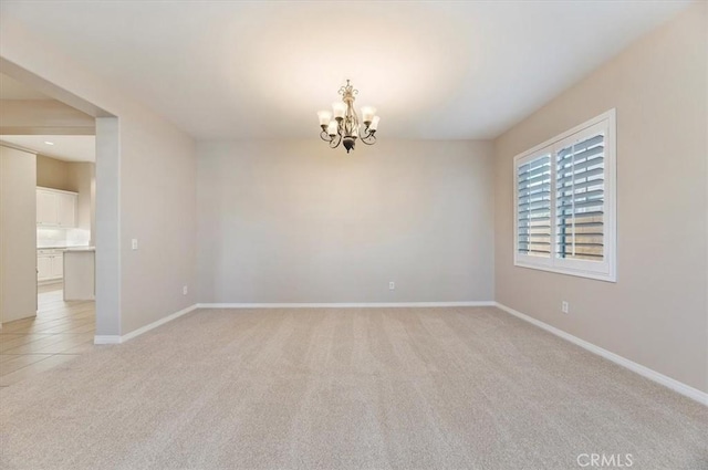 spare room with light carpet, baseboards, and a notable chandelier