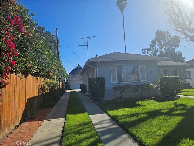 view of front facade featuring stucco siding, fence, and a front yard